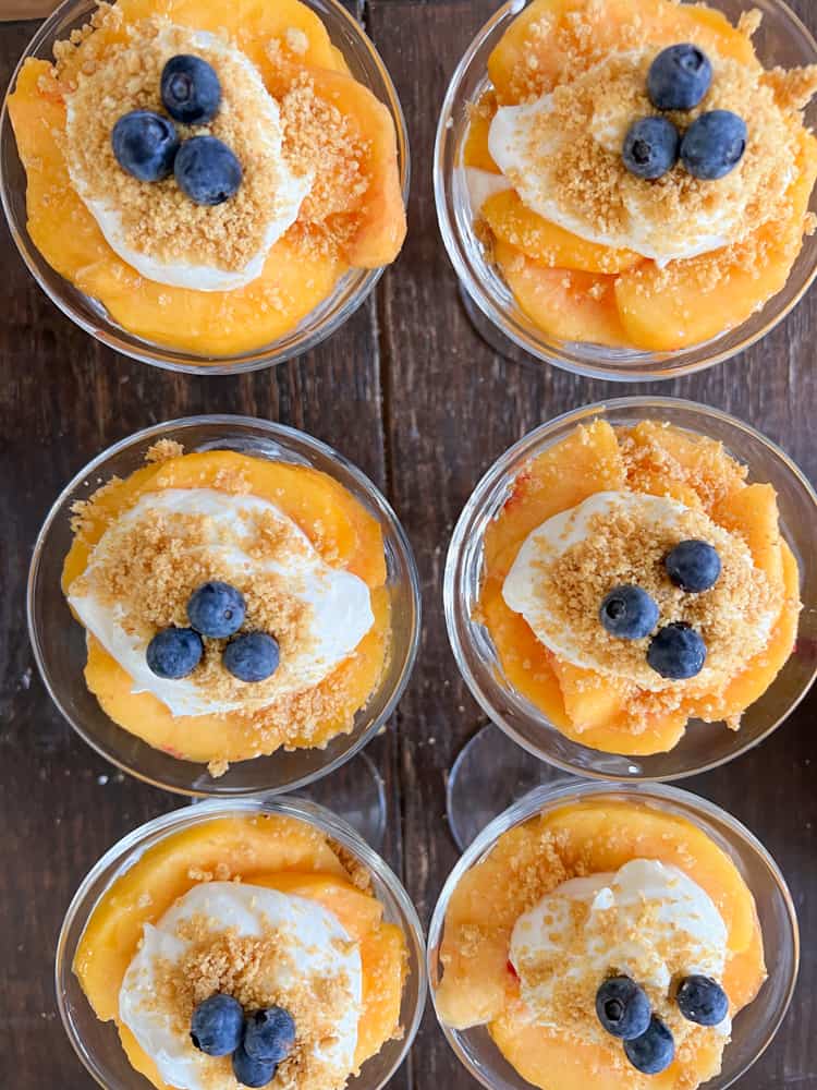 Top dreamy peaches & cream parfait dessert with graham cracker crumbs & fresh blueberries. 