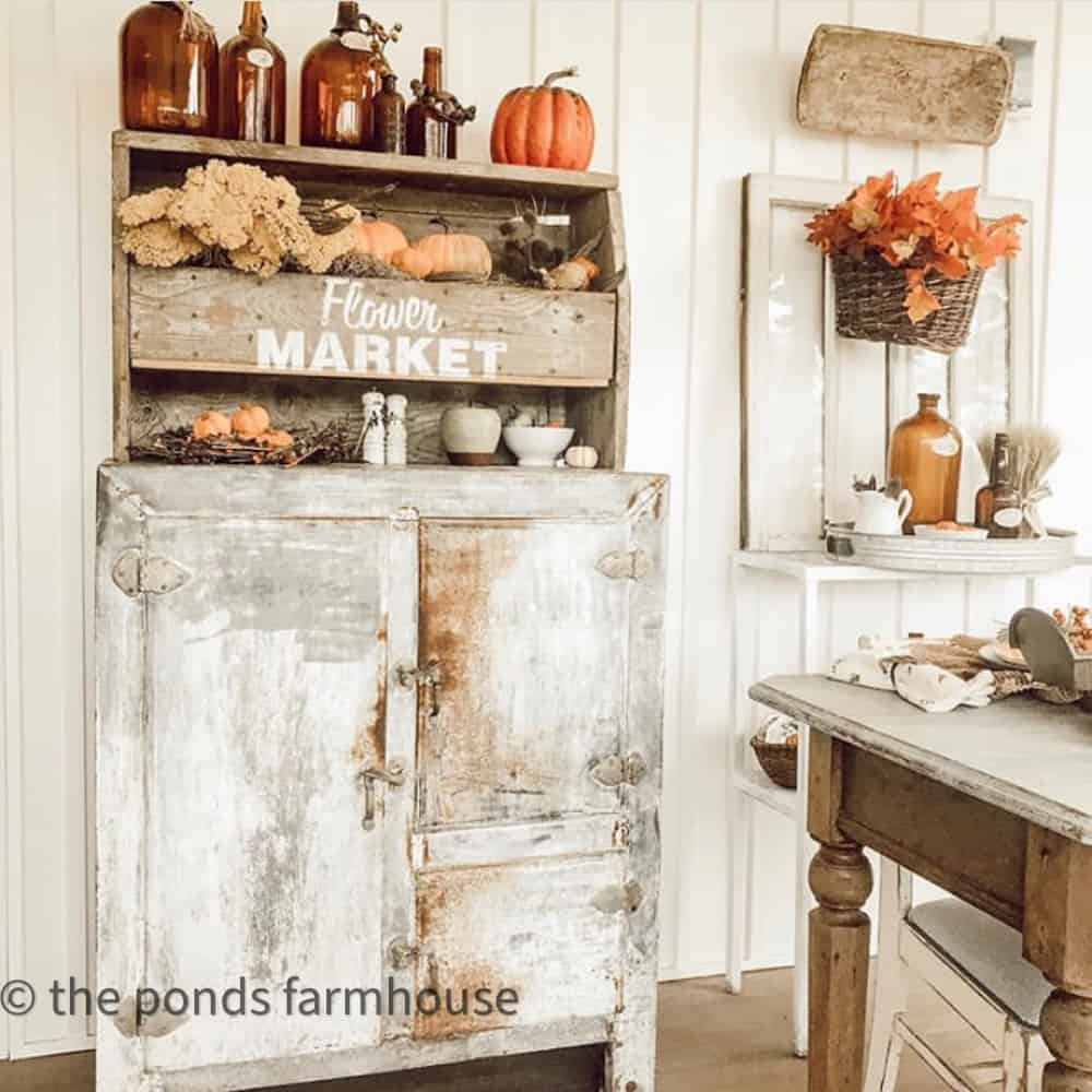 Screened Porch cabinet filled with fall decor such as amber bottles and pumpkins on a vintage ice box. 