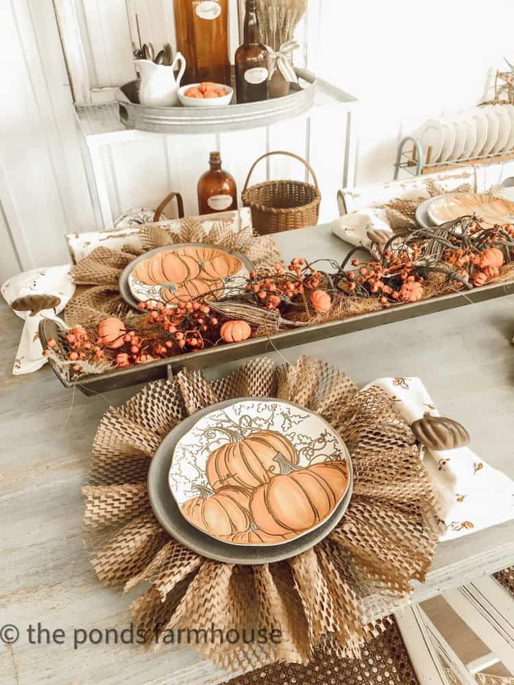 A metal tray centerpiece filled with fall stems, dried okra pods and mini pumpkins along with packing material DIY Plate Chargers