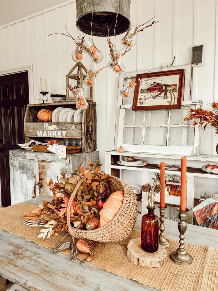 Basket and pumpkin centerpiece on screened porch table with orange candles.  