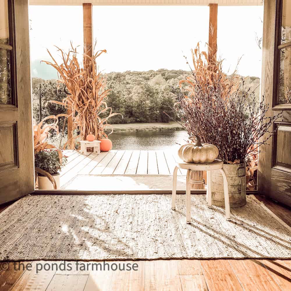 Pond view of the farmhouse front porch with cornstalks, pumpkins and pussy willow stems for fall decorating.