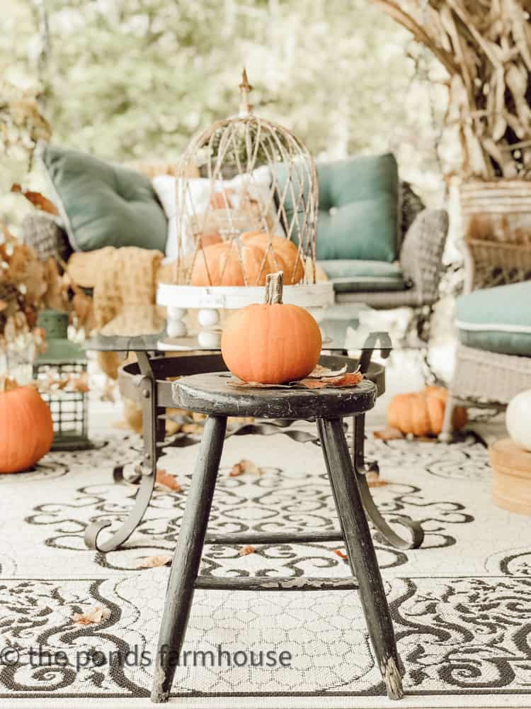 Single pumpkin on vintage black stool for farmhouse front porch decorating ideas. 