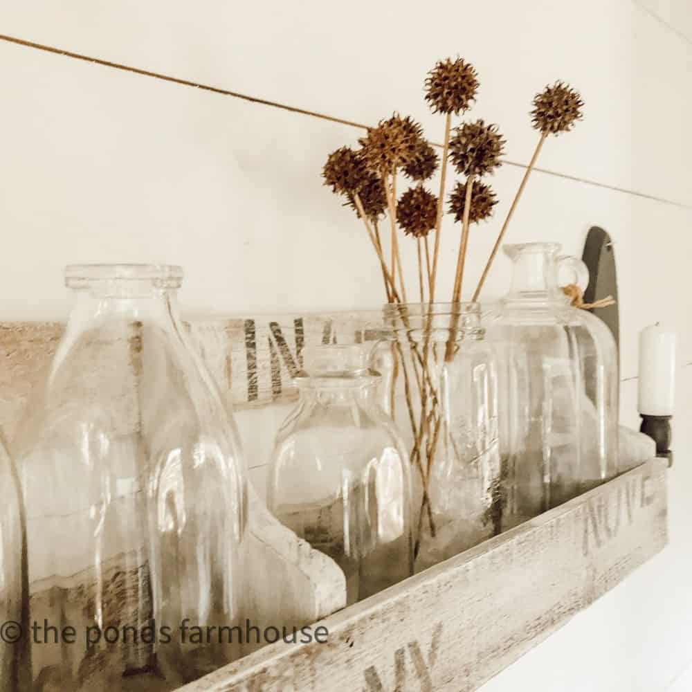 Vintage old milk bottles with sweet gum ball stems in a wooden rack for fall decorating.