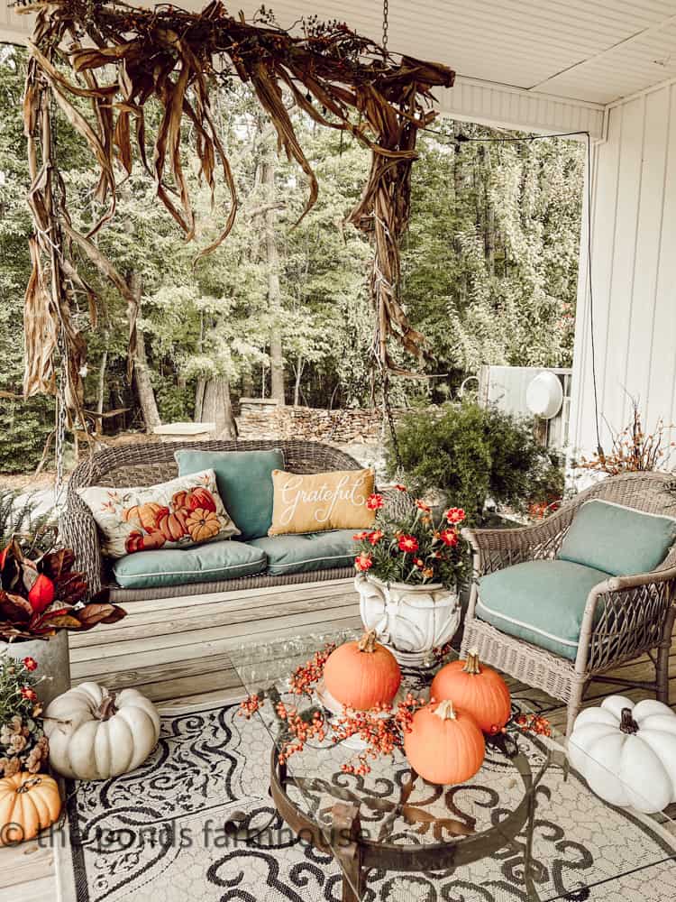 Farmhouse front porch ideas with porch swing and corn stalk garland with cozy throw pillows & pumpkins
