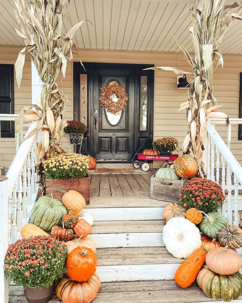 Porch steps filled with pumpkins and mums.  corn stalks and  vintage wagon for fall