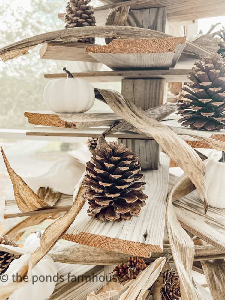 Shiplap tree with pinecones, corn stalks, and pumpkins for rustic porch decor.