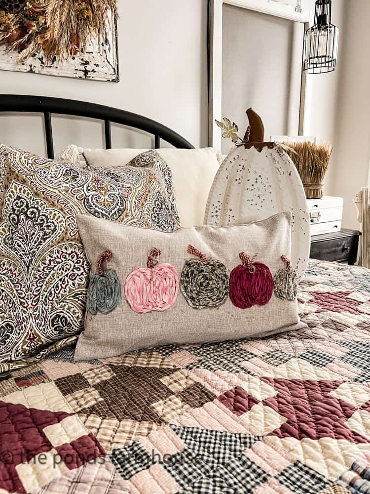 DIY scrap fabric pillow with pumpkins for a fall pillow cover rests on the vintage yard sale quilt.