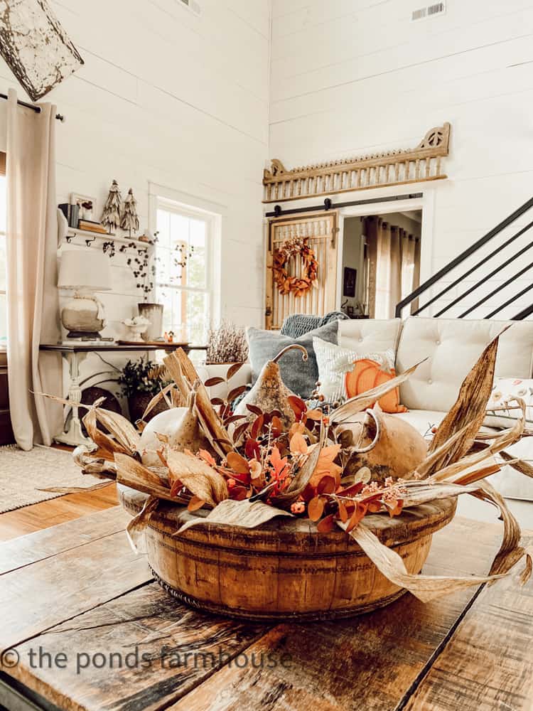 Large wooden bowl is filled with corn stalk decorations and dried gourds.