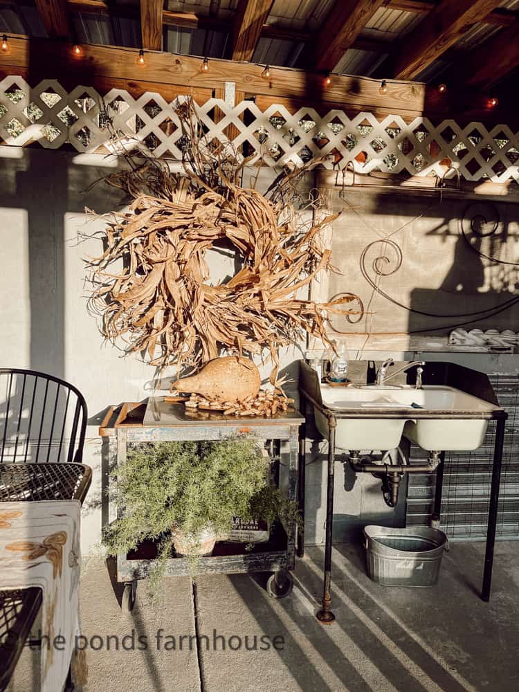 Vintage screen door hangs above the sink in the outdoor kitchen.  The DIY Corn Husk Wreath decorates the area for fall.
