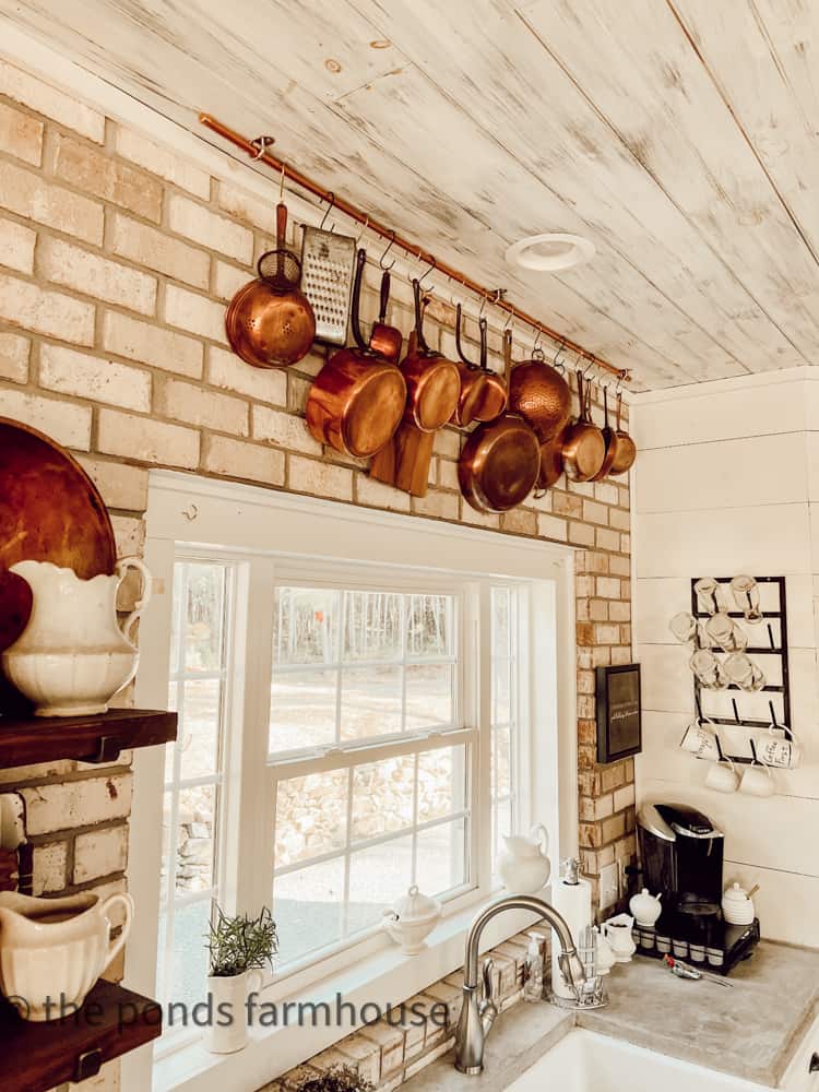 Vintage Copper hangs on a brick wall with DIY copper pot hanging rack. Sustainable Farmhouse Decorating Ideas. 