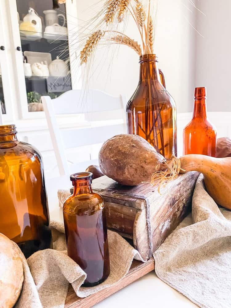 Rustic Thanksgiving Table Centerpiece with Amber Bottles and Dried Gourds.