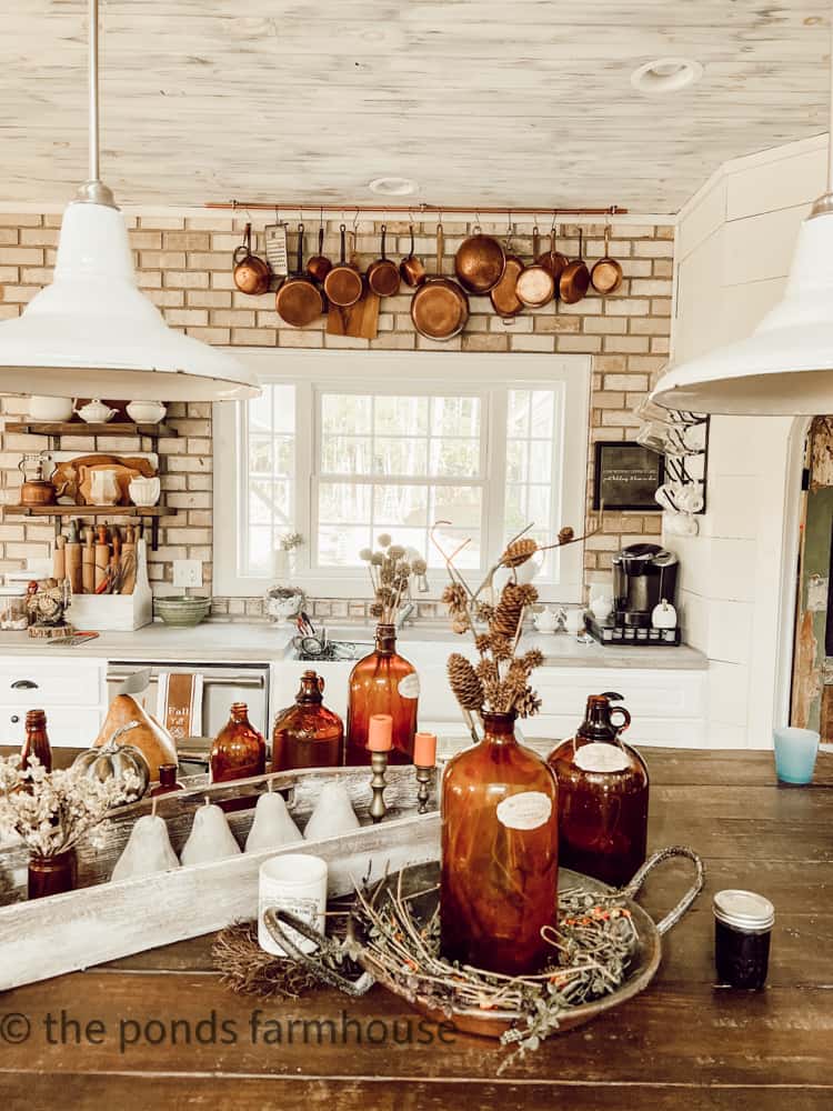 Copper Pot collection hanging on brick wall with amber bottler for fall dccorating.