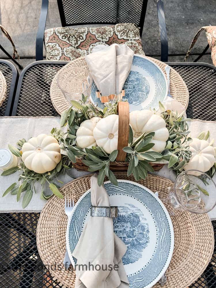Small white pumpkins fill a narrow basket with fresh sage for a fall centerpiece on the narrow bistro tables