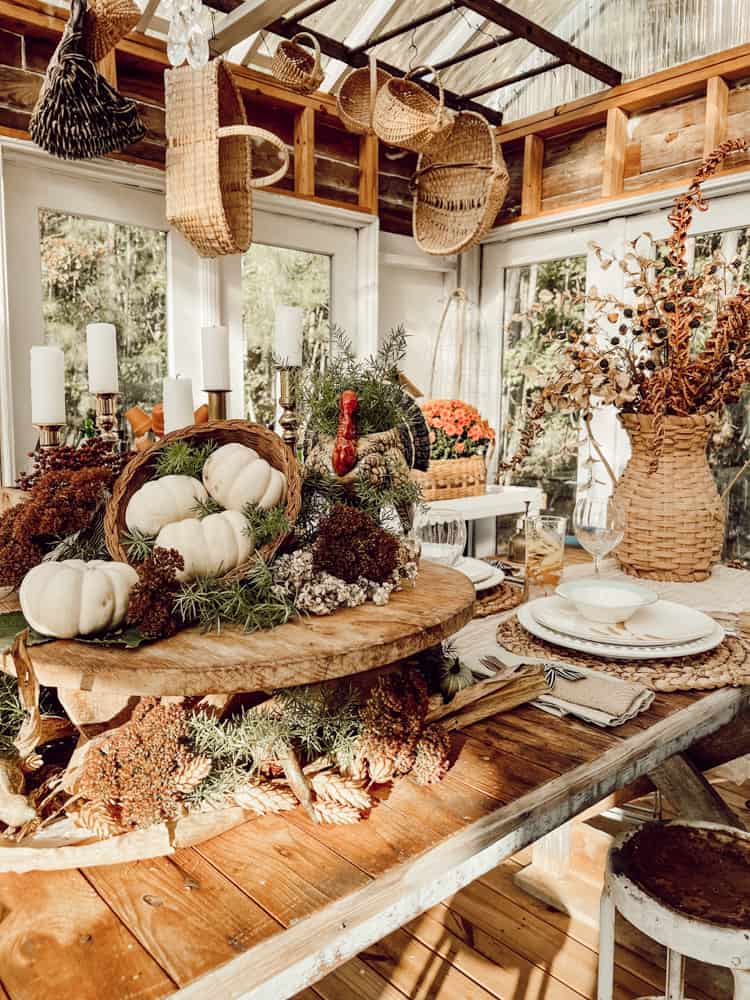 Greenhouse/She-shed Friendsgiving table centerpiece ideas with cheese board riser and white pumpkins.