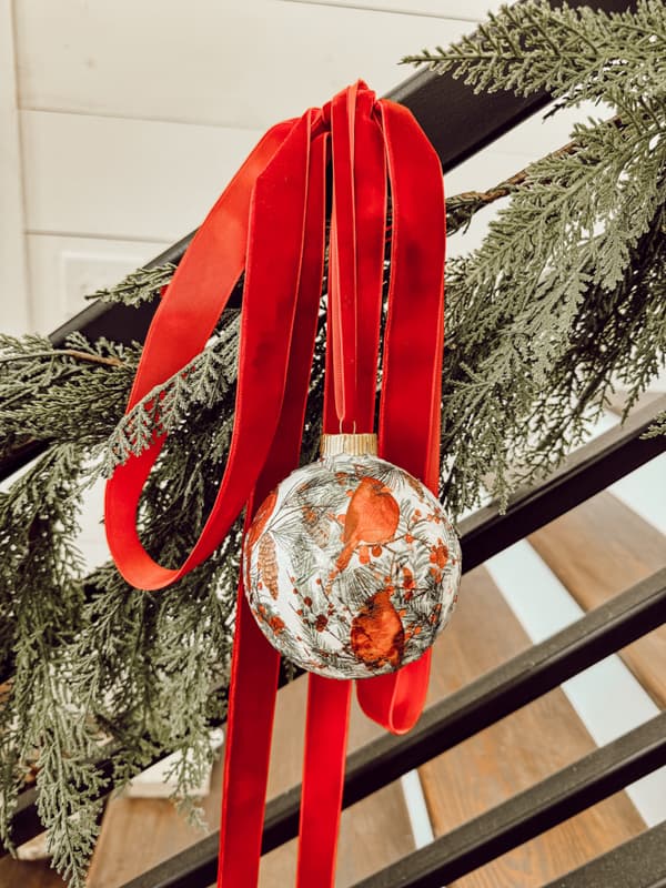 Opaque REd Bird Napkin Decoupage Christmas Ornament with red ribbon on iron banister railing.  