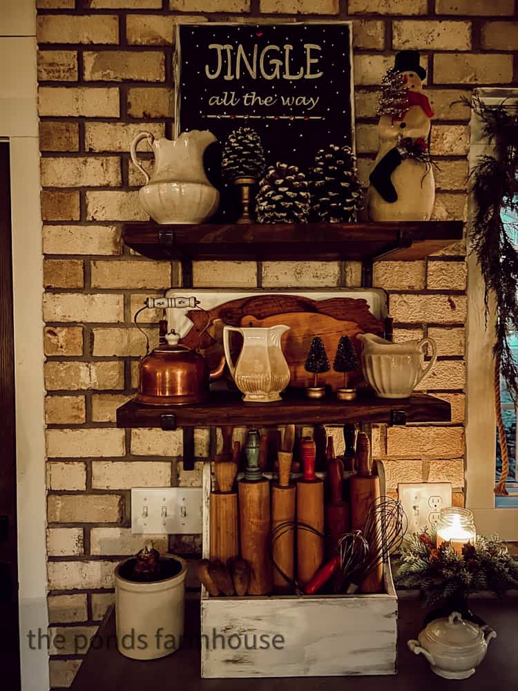 OPen shelving in farmhouse kitchen with Christmas decorations and vintage rolling pin, pig cutting boards, ironstone.