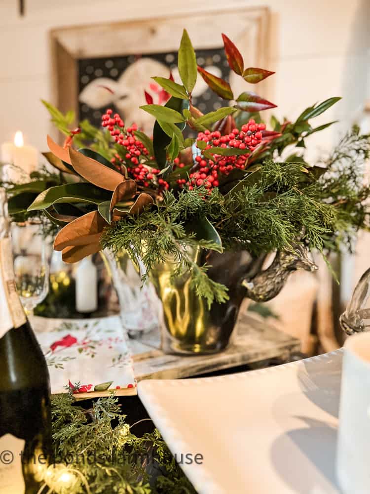 Pewter container filled with fresh greenery, cedar, magnolia leaves, and Nandina with red berries.for Farmhouse Centerpiece