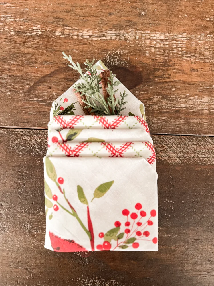 Cutlery Pocket Napkin Fold with reversible red bird napkins and greenery and cinnamon sticks.