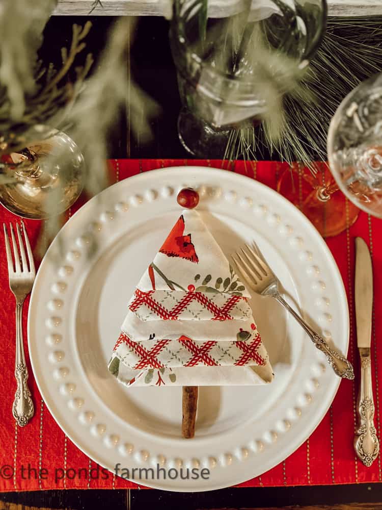 DIY Christmas Tree Napkin Fold with cinnamon stick trunk and cranberry topper.