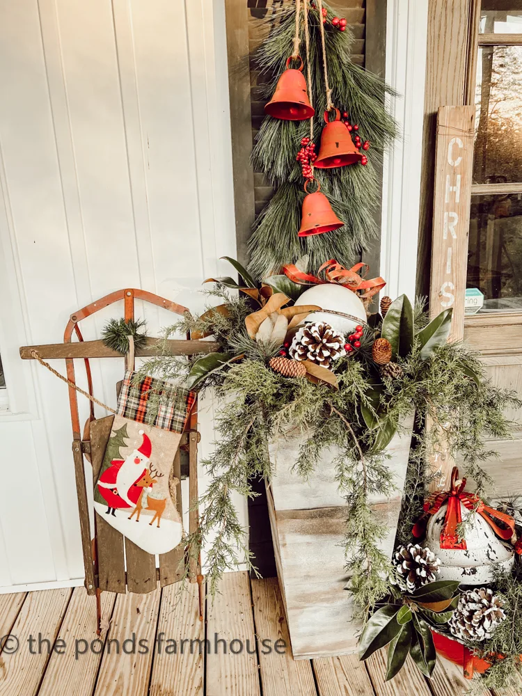 Vintage sleigh, red and white bells, and greenery fill the DIY planters for Farmhouse Porch Decorated for Christmas