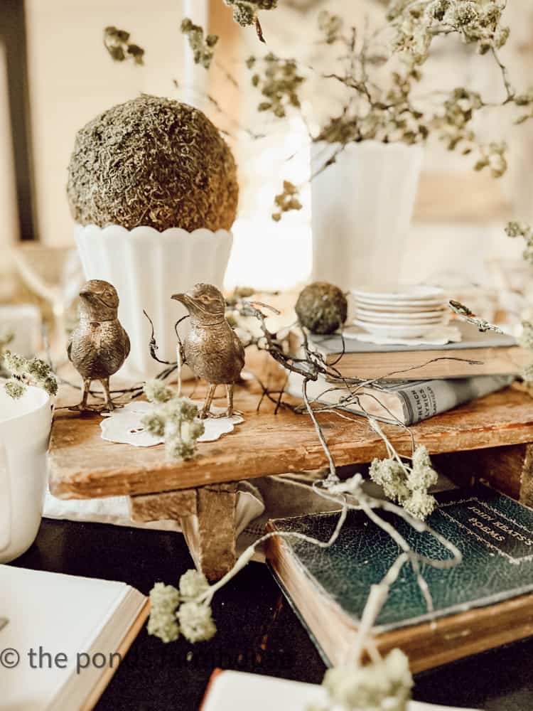 Book Club Brunch Tablescape filled with preserve moss balls and vintage cheese board with old books & brass birds.