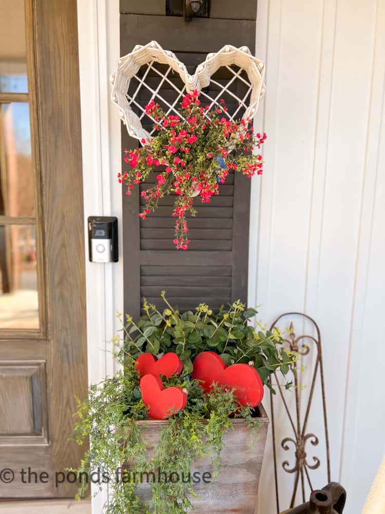 Thrifted basket with flowers on black shutter and planter filled with greenery and wooden hearts. 