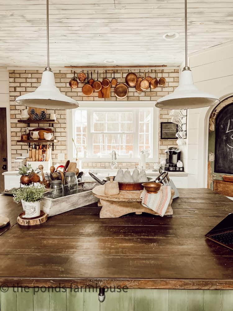 DIY Farmhouse Kitchen Island with brick backsplash and vintage copper pots on a pot hanger rack.