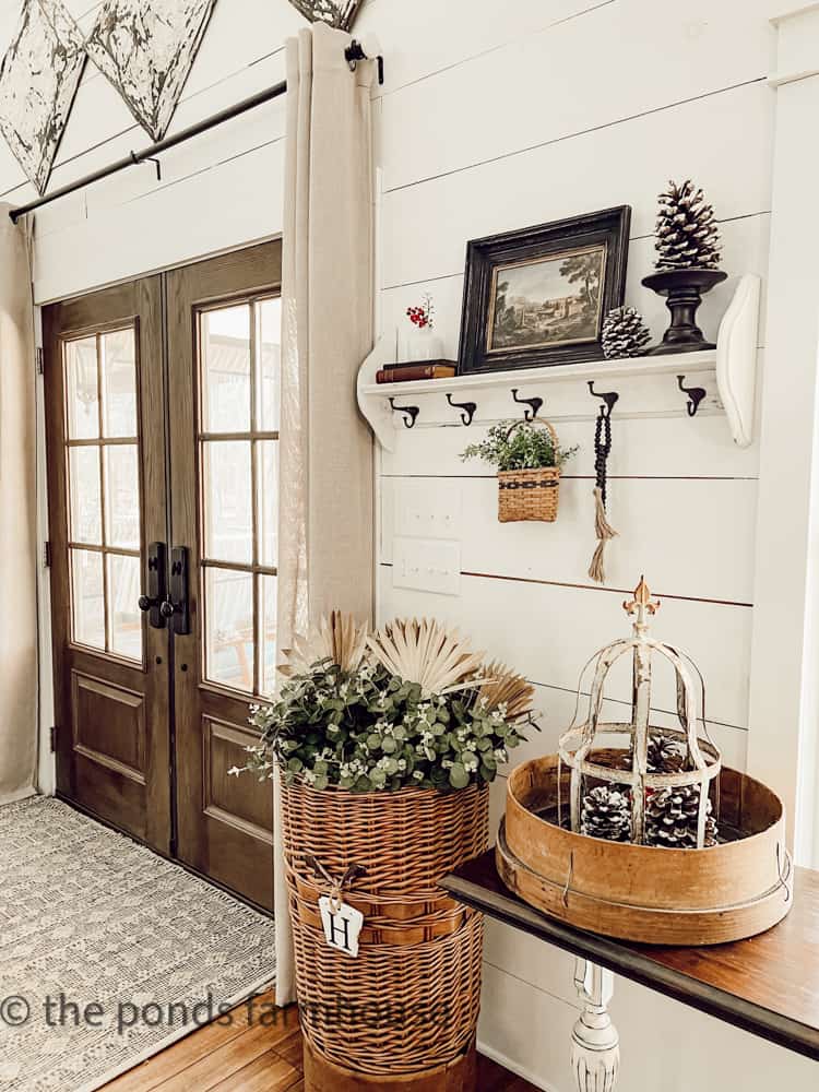 French doors at farmhouse entry with basket of greenery and foraged pinecones.