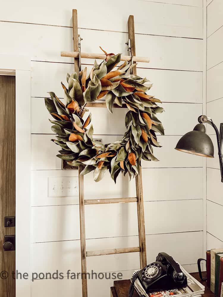 DIY Magnolia Wreath on a vintage ladder against Shiplap wall in cozy winter farmhouse.