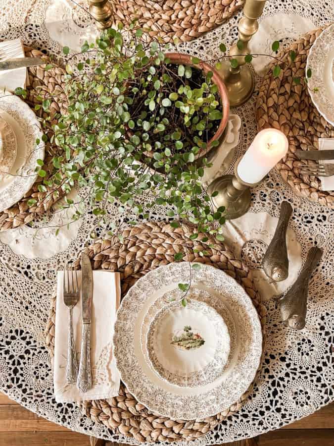 Winter Tablescape with green vine and brass candlesticks, bird salt and pepper shakers and thrift store dishes.