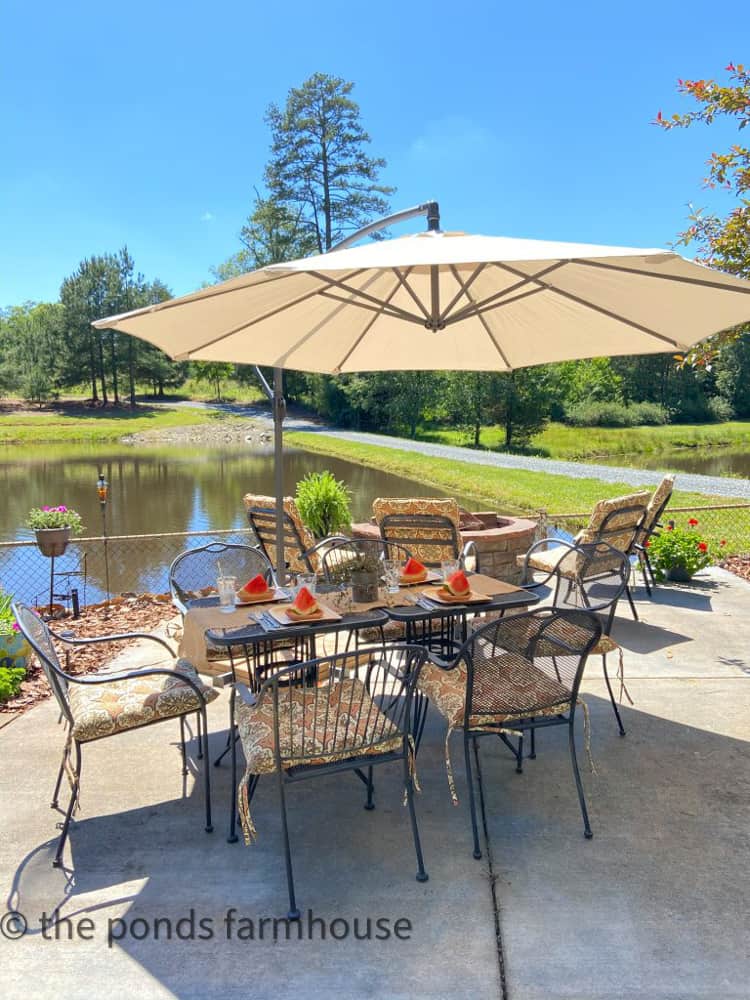 Alfresco dining table with umbrella by fire pit and beside the pond.