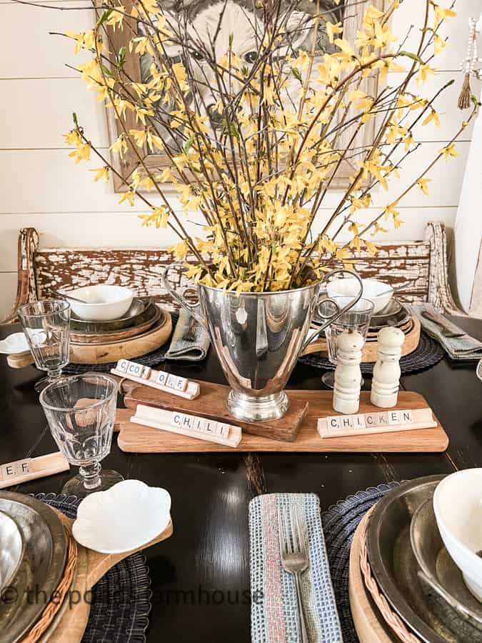 Rustic Table Centerpiece with scrabble tiles, vintage breadboards, silver urn with forced forsythia blooms.