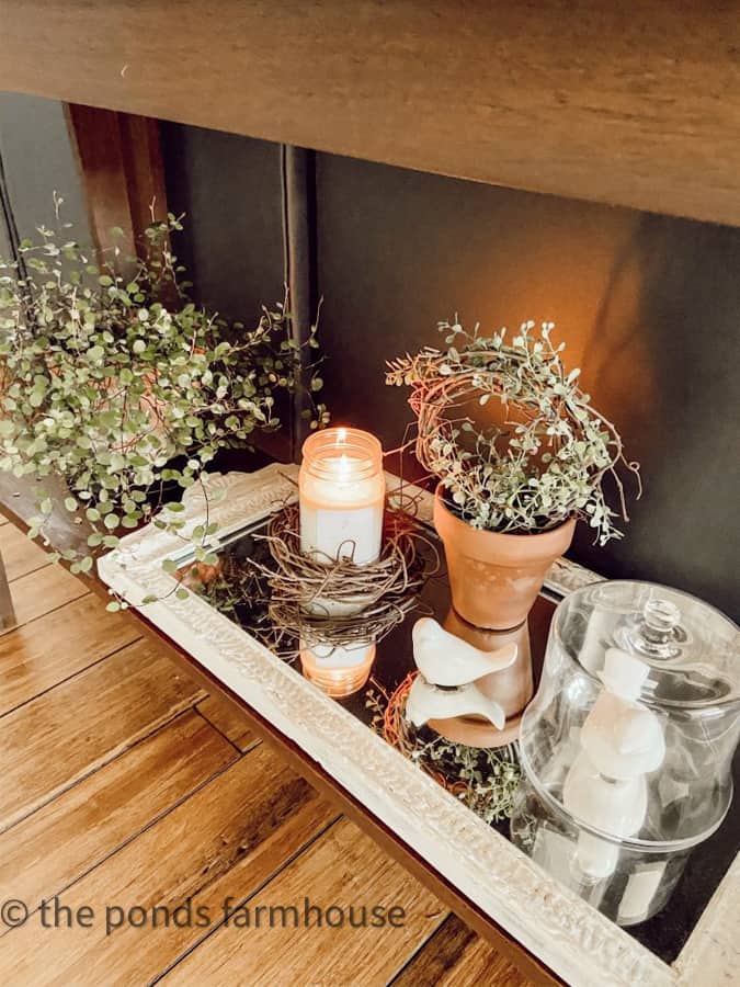 Lower shelf of Sofa Table decorated with mirror, greenery and candles.