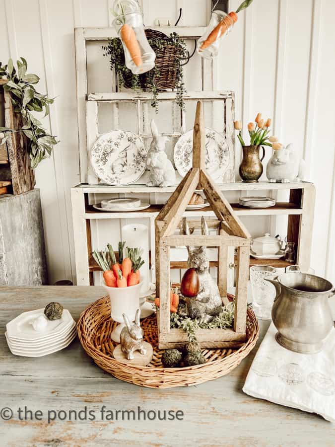 Full Spring Table Centerpiece with woven basket, tobacco stick lantern, Dollar Tree carrots, pewter bunnies, ironstone plates and pewter pitcher.