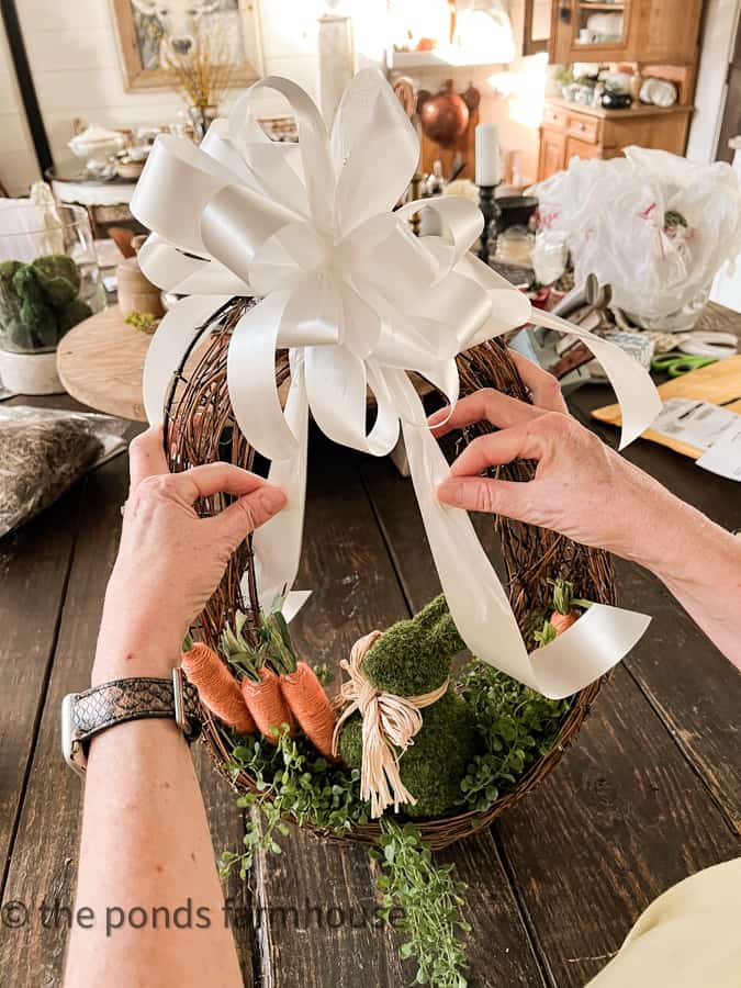 Making an Easter wreath with a white satin bow is optional.  Egg Shaped Wreath with bunny, carrots and greenery