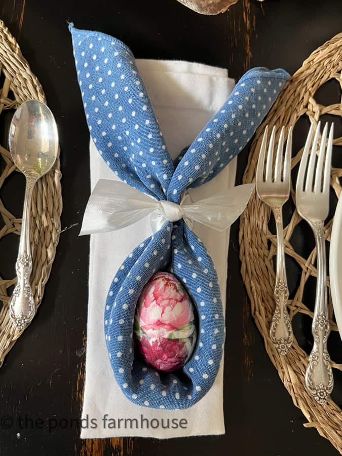 Bunny Ears Folded Napkins on Easter Table with decoupage Easter eggs  on a white folded napkin at place setting.