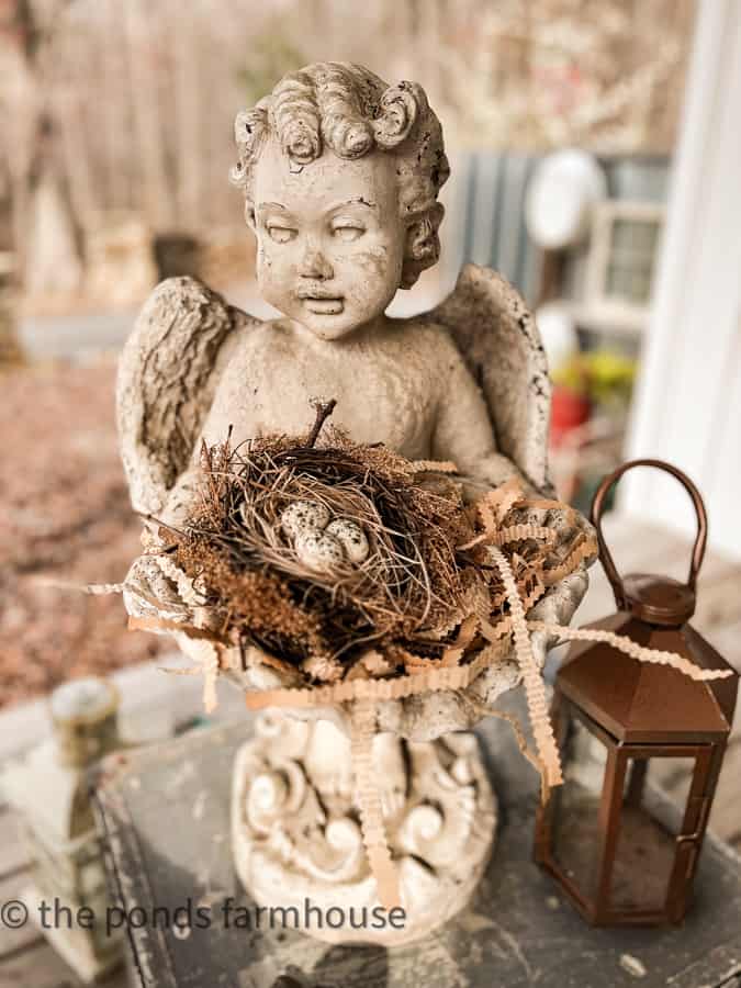 Easter Outdoor Decor idea is to add a bird nest with eggs to the concrete angels hands on the front porch.