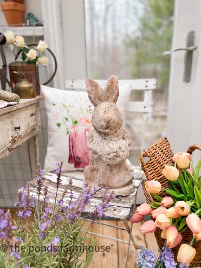 Garden decorations - chippy concrete bunny in greenhouse surrounded by flowers. Vintage Garden Statuary 