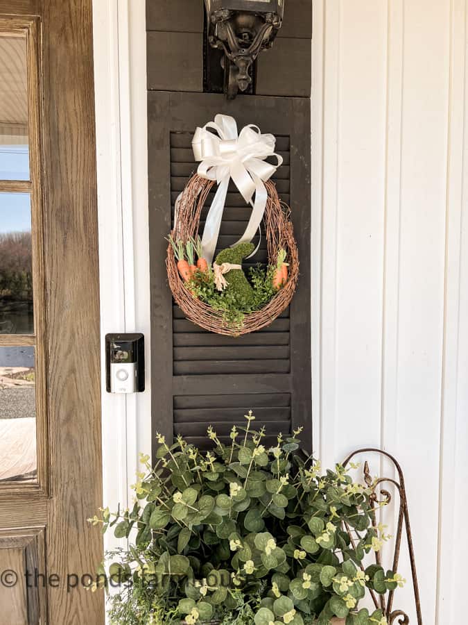 DIY Easter Wreath hanging on DIY Door Shutters with planter filled with faux greenery.  Farmhouse Style Wreath