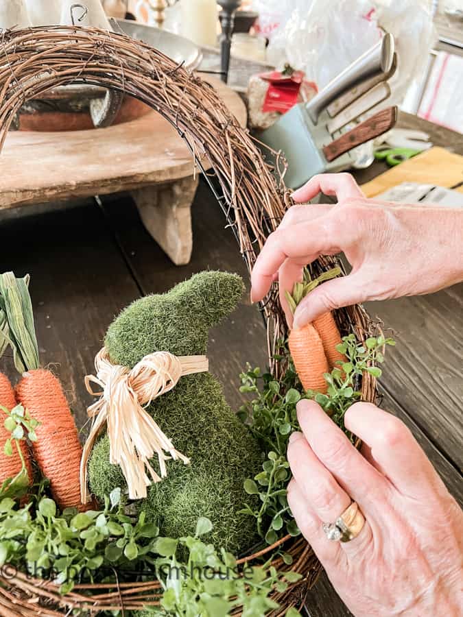 Add faux carrots from Dollar Tree  to the Easter Wreath DIY.  Oval Wreath with artificial greenery, moss bunny and carrots.