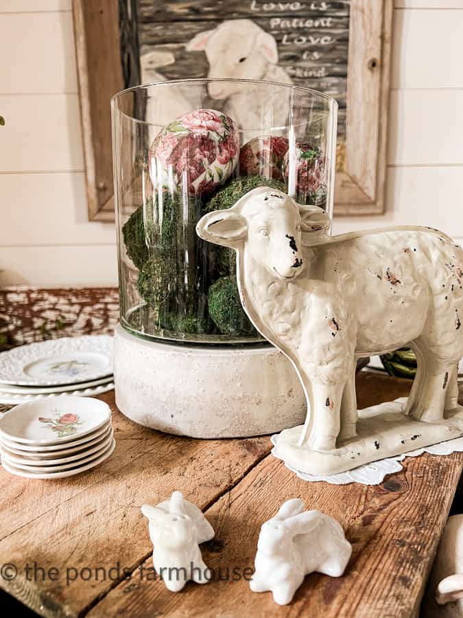 Decorated Easter Table Centerpiece with hurricane lantern filled with moss and decoupage easter eggs with lamb.