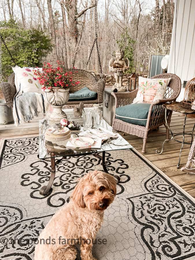 Seating area on farmhouse front porch with wicker furniture and a coffee table filled with Easter Dishes.  