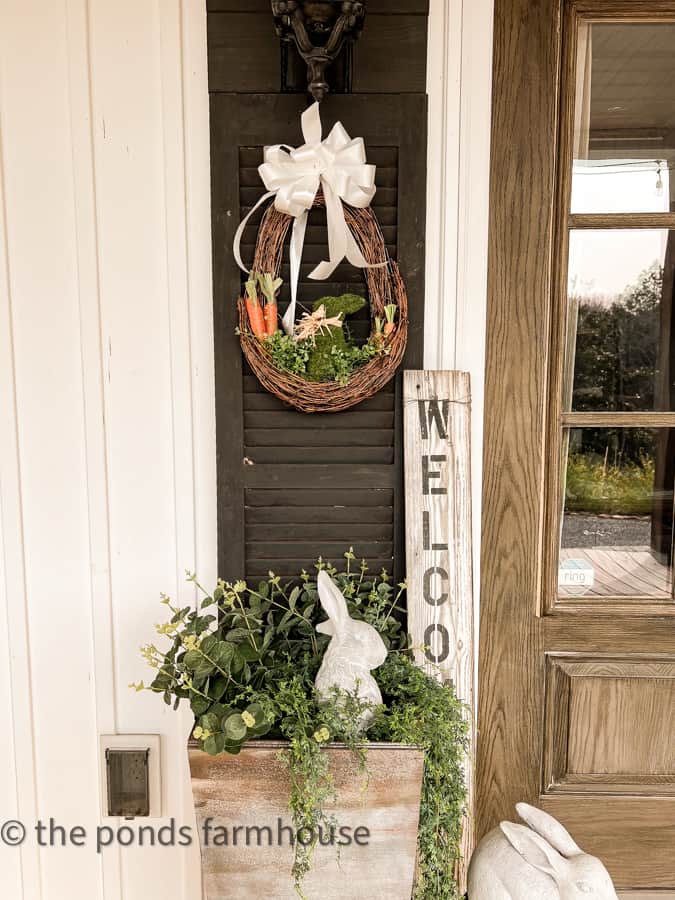 DIY Easter Wreath with moss bunny and carrots over a DIY planter with greenery and concrete bunny for porch decor.