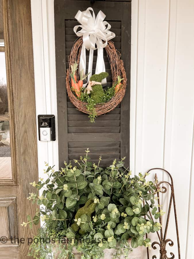 DIY Easter Wreath with moss bunny and carrots over a DIY planter with greenery Ideas to Decorate For Easter on porch.