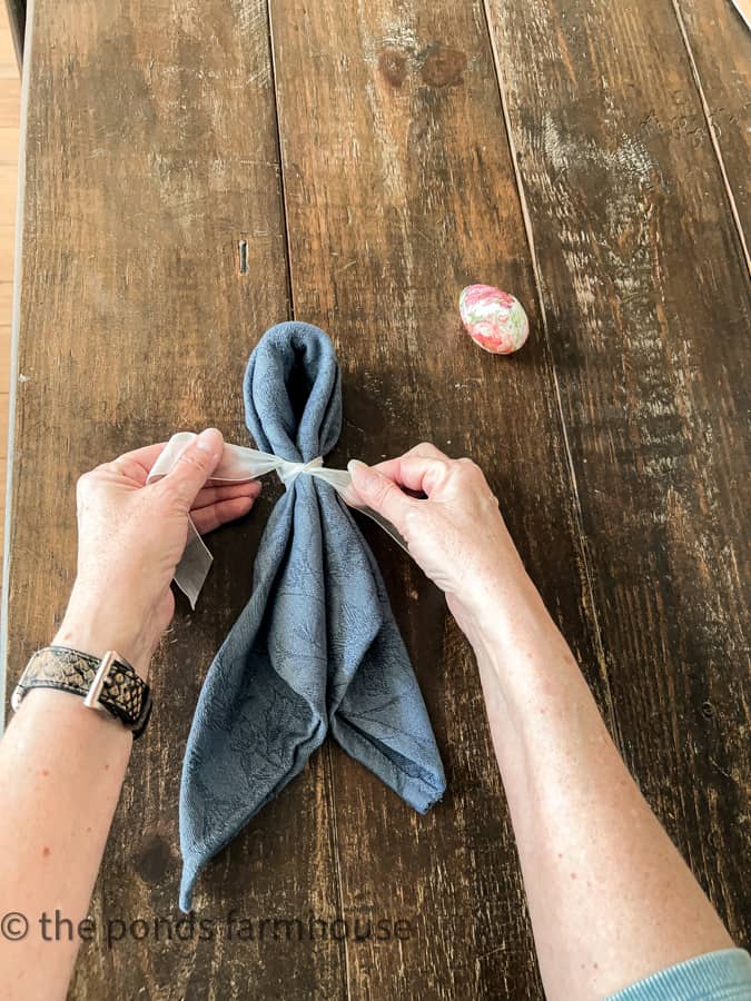 Tie ribbon around folded napkin to make A Bunny Ear Napkin Fold for Easter Table Settings. 