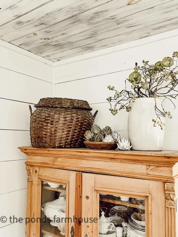 thrifted vintage basket and old crock fill top of natural pine hutch for country chic decorating ideas.