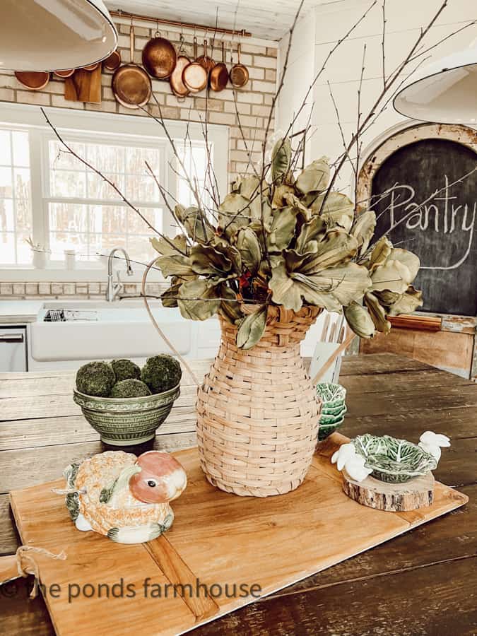 Kitchen Island Centerpiece with larger breadboard, handwoven basket vase with twigs and faux flowers.