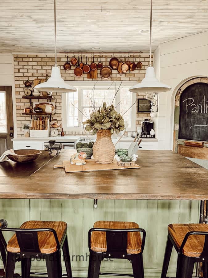 DIY kitchen island painted green with rustic pantry door and shiplap walls.  Brick backsplash with Vintage Copper Hanging Pots.  