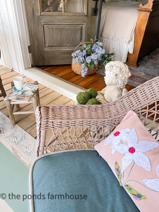 Accessories for porch sitting with baskets of flowers, concrete angel with moss balls and wicker furniture.