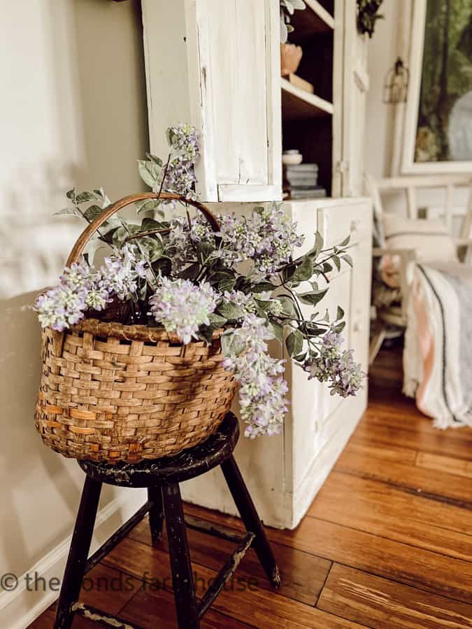Inexpensive thrift store bassket on wooden stool filled with fresh lilacs.  